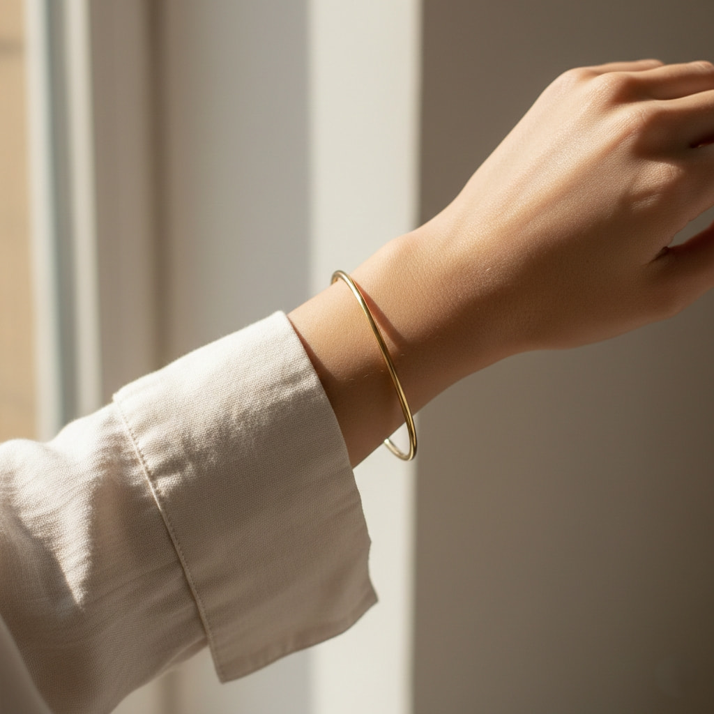 Thin gold bangle bracelet minimal jewelry for daily wear on woman's wrist with neutral clothing